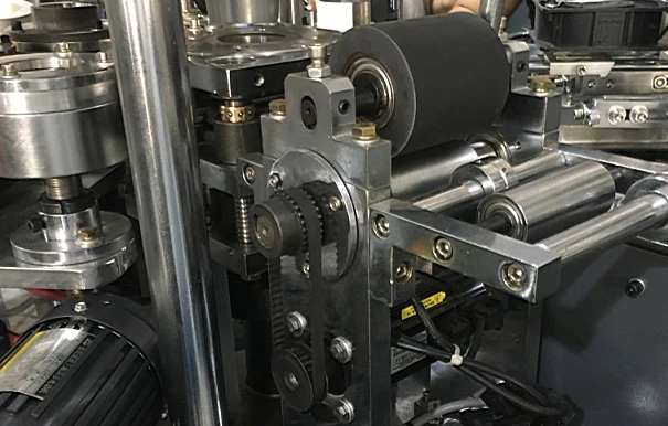 Detalhe dos rolos de alimentação do papel do fundo e do mecanismo de acionamento da máquina de copos de papel ZBJ-OC12; fotografia estática do equipamento fornecida.